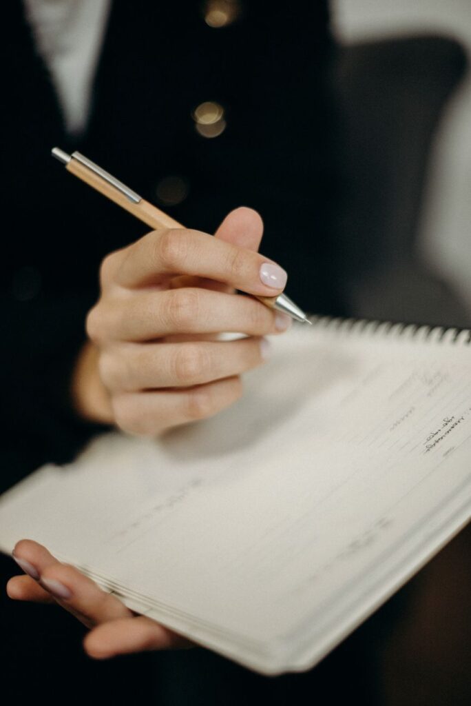 person holding orange click pen writing on notebook