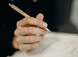 person holding orange click pen writing on notebook